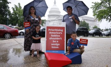 A family poses in front of the U.S. Capitol building with signs saying Think Babies.